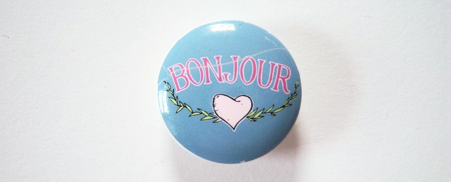 Round blue and in white script Bonjour with white heart and vine 15/16" with shank back poly button.